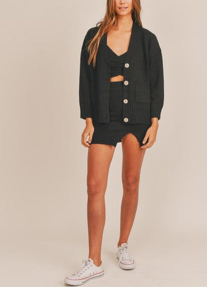 Black 3 piece sweater set with spaghetti strap crop top, mini slit skirt, and long sleeve button cardigan.